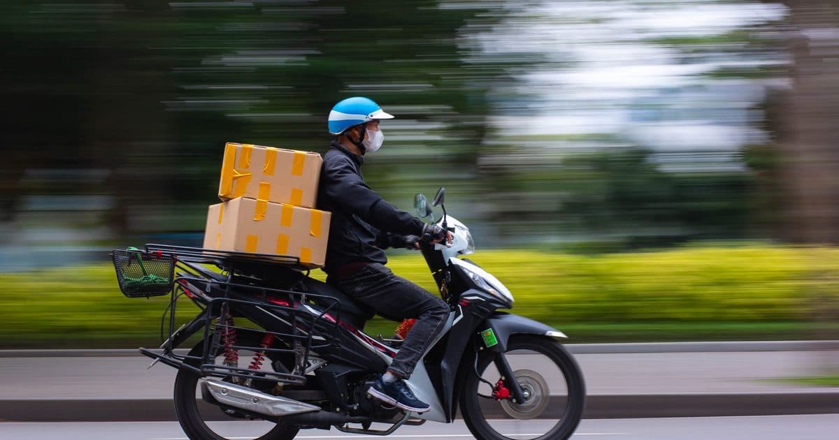 A delivery rider on a scooter carrying cardboard boxes through the city.