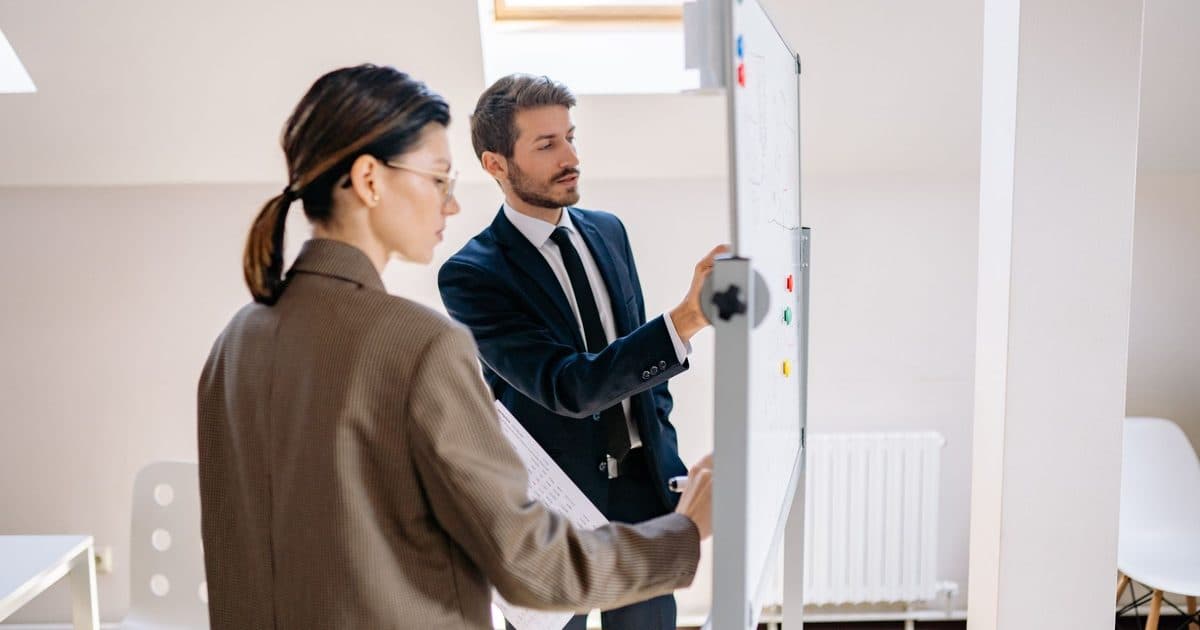 Two colleagues discussing strategies at a whiteboard in an office.