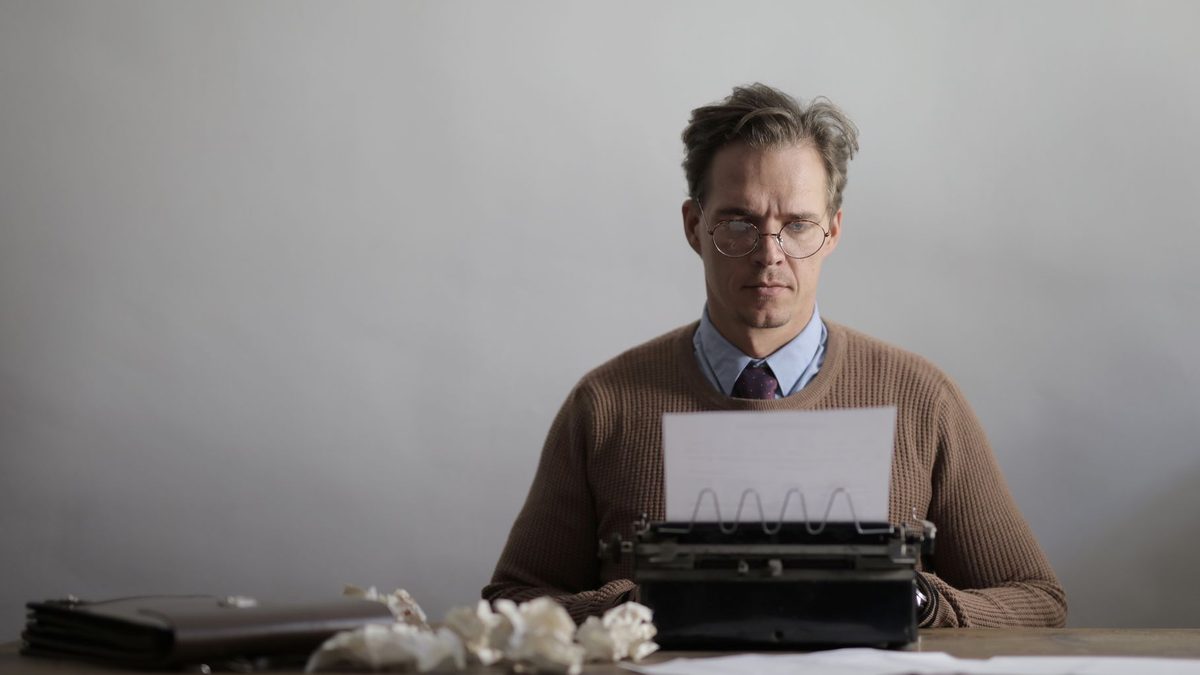 A writer typing on a typewriter surrounded by papers.