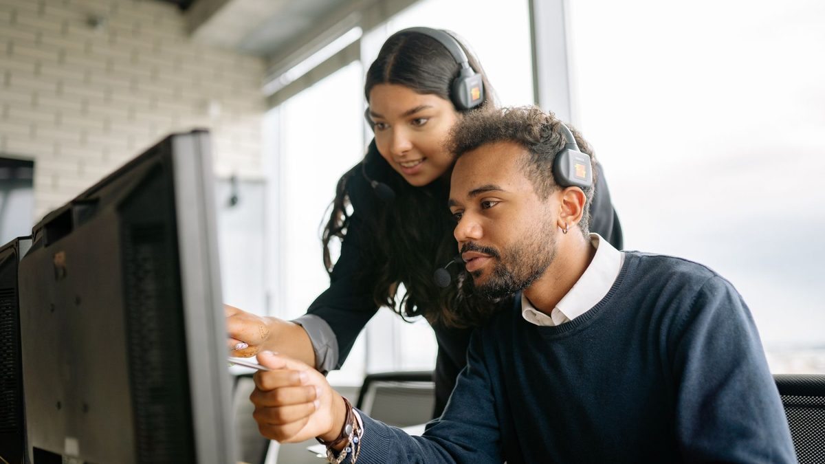 Two support agents wearing headsets working at monitors.