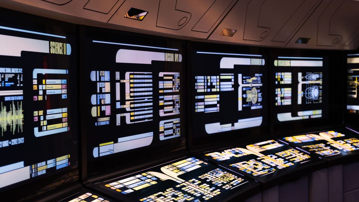 A control room with multiple illuminated screens.