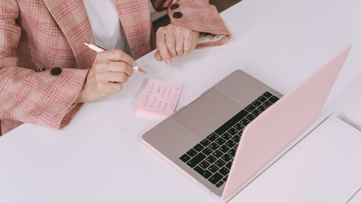 A person taking notes next to a laptop in a meeting.