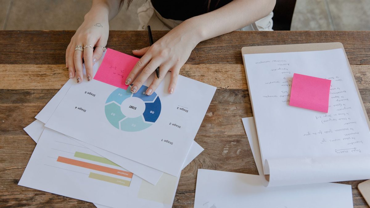Hands arranging charts and sticky notes on a desk.
